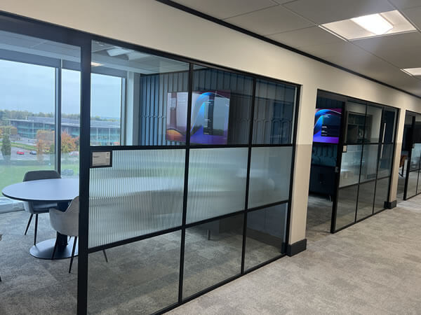 View of Synextra’s meeting rooms with glass partitions and Sony displays showing Teams Room interfaces installed by Rapid Technologies.